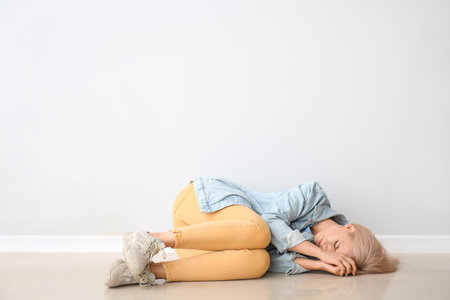 Stressed young woman lying near light wallの写真素材