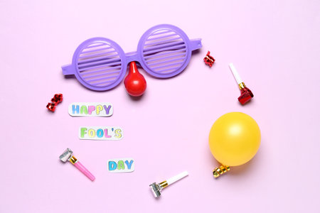 Frame made of text HAPPY FOOL'S DAY, funny disguise, balloon and party blowers on pink background