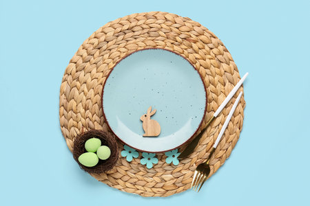 Table setting with cutlery, bunny and Easter eggs in nest on blue backgroundの写真素材