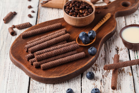 Board with delicious chocolate wafer rolls, coffee beans, condensed milk and blueberries on white wooden backgroundの写真素材