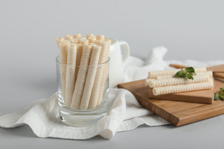 Board and glass with delicious wafer rolls and mint on gray backgroundの写真素材