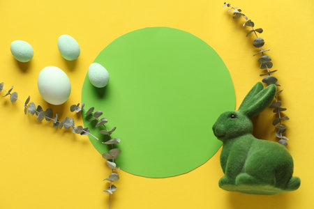 Blank greeting card, painted eggs, Easter bunny and eucalyptus branches on yellow backgroundの写真素材