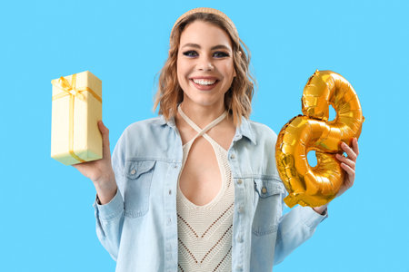 Happy young woman with balloon in shape of figure 8 and gift on blue background. International...