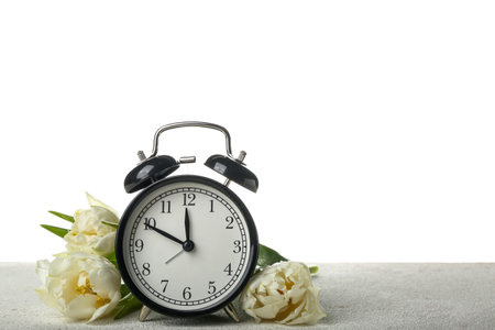 Alarm clock with beautiful tulip flowers on table against white background