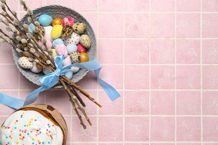 Bowl of beautiful Easter eggs, willow branches and tasty cake on color tile