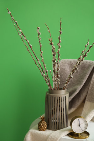Vase with willow branches, decor and alarm clock on chair near green wallの写真素材