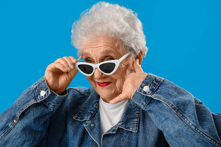 Senior woman in sunglasses showing call me gesture on blue background, closeup