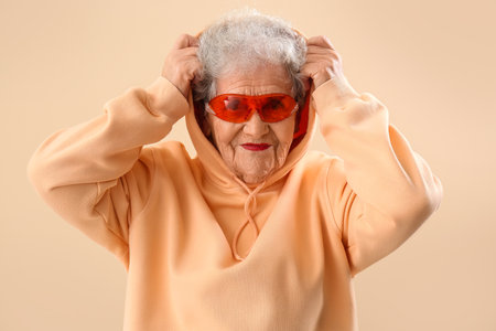 Senior woman in sunglasses and hoodie on beige backgroundの写真素材