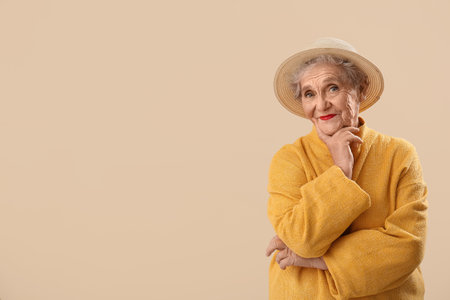 Thinking senior woman in hat on beige backgroundの写真素材
