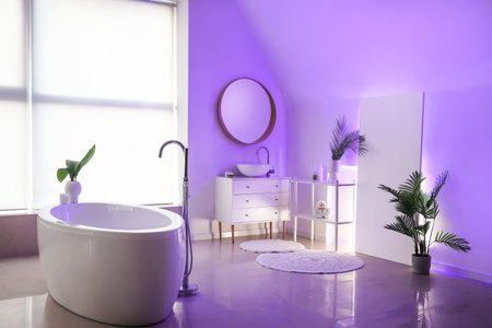 Interior of stylish bathroom with bathtub, houseplants, mirror and neon lightingの写真素材