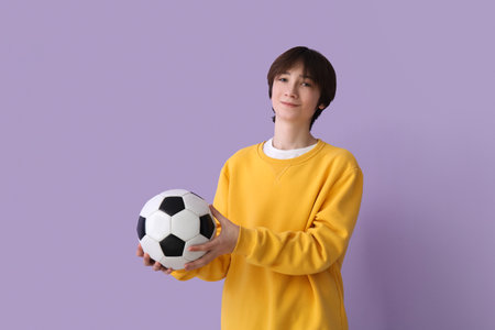 Teenage boy with soccer ball on lilac backgroundの写真素材