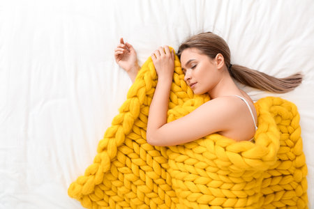 Happy young woman with warm plaid lying on bed, top viewの写真素材