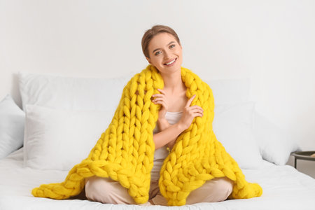 Happy young woman with warm plaid at homeの写真素材