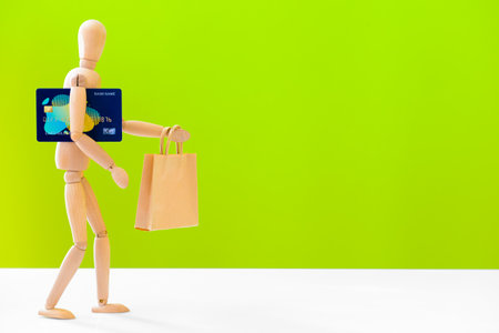 Wooden mannequin with shopping bag and credit card on color backgroundの写真素材