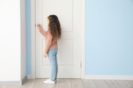 Cute little girl standing near closed doorの写真素材