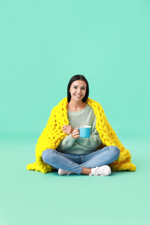 Beautiful young woman with warm plaid and tea on color backgroundの写真素材