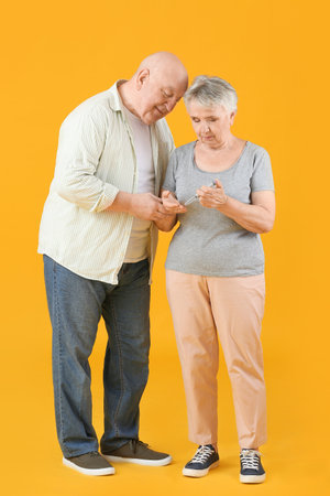 Senior diabetic couple with lancet pen on color backgroundの写真素材