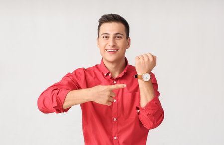 Young man with wristwatch on light backgroundの写真素材