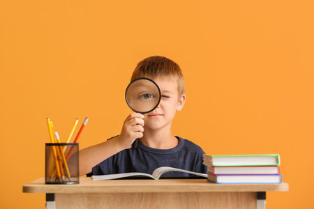 Cute pupil sitting at desk against color backgroundの写真素材