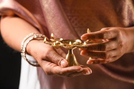 Woman holding diya lamp for celebration of Divaly on dark background, closeup