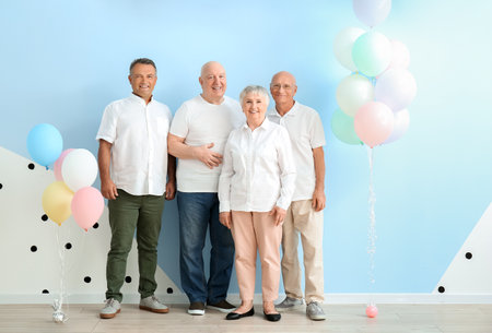 Senior people with balloons near color wall in room
