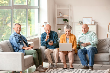 Senior people with different devices sitting on sofa at home