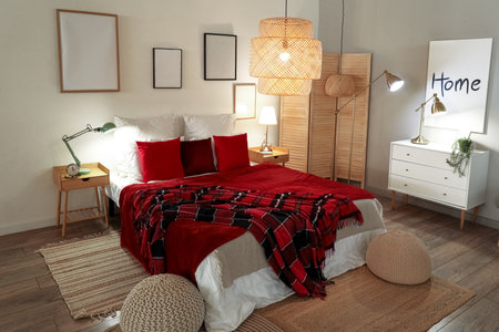 Interior of bedroom with red checkered blankets on bed and glowing lamps late in the eveningの写真素材