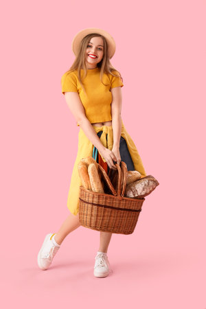 Young woman in hat with basket of fresh bread on pink backgroundの写真素材