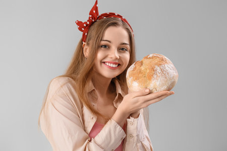 Young woman with fresh bread on gray backgroundの写真素材