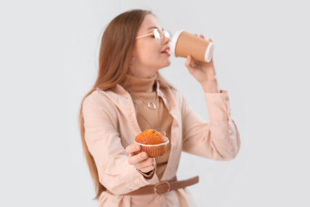 Young woman with tasty cupcake drinking coffee on light background