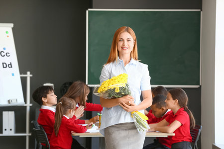 Beautiful teacher with bouquet of flowers in classroomの写真素材