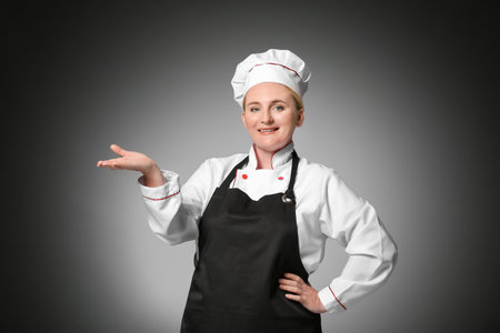 Mature female chef showing something on dark backgroundの写真素材