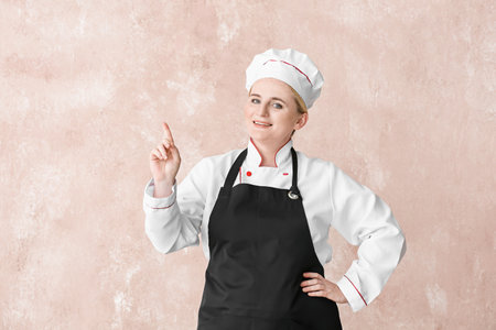 Mature female chef pointing at something on color backgroundの写真素材