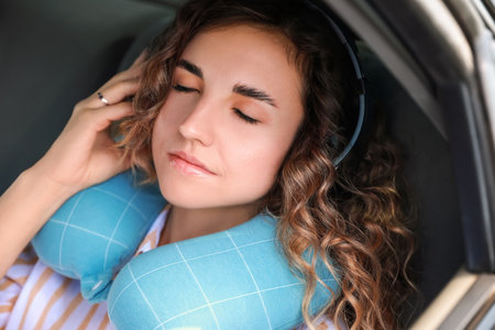 Beautiful young woman with travel pillow and headphones sleeping in car
