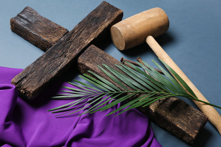 Cross with palm leaf, hammer and purple fabric on blue background, closeup. good friday concept