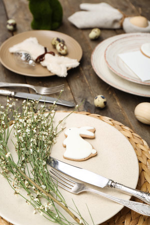Table setting with Easter eggs, bunny and flowers on wooden background, closeup