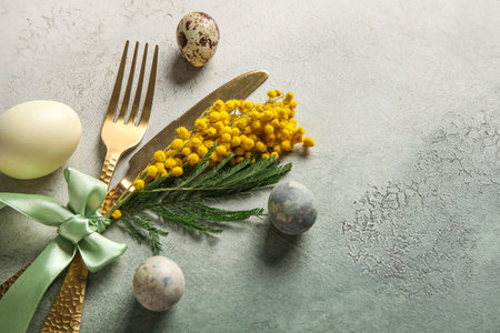 Table serving with Easter eggs and mimosa flowers on gray grunge background