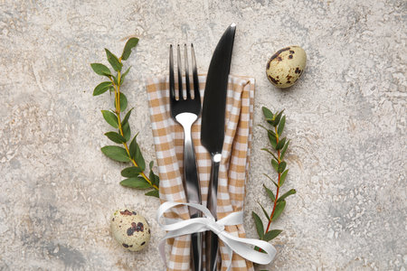 Cutlery with napkin, Easter eggs and plant branches on grunge background, closeup
