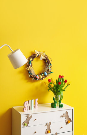 Chest of drawers with tulips in vase, rabbits and Easter wreath on yellow wallの写真素材