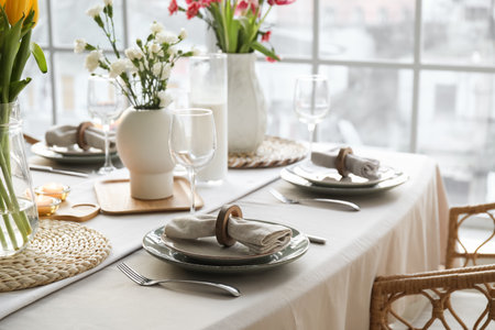 Beautiful table setting for International Women's Day celebration with flowers in light room near...