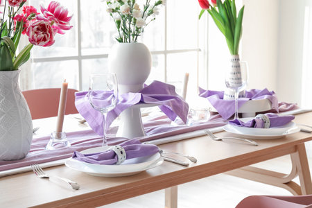 Beautiful table setting for International Women's Day celebration with different flowers and burning candles in light room near windowの写真素材