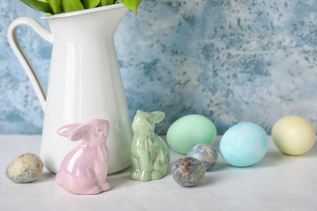 Easter bunnies, vase and painted eggs on table near blue grunge wall