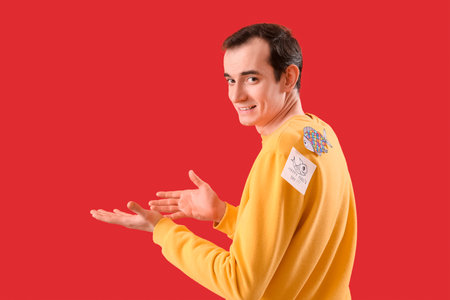 Sticky paper with text HAPPY FOOL'S DAY and fish on young man's back against red background