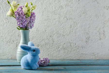Vase with beautiful flowers and Easter bunny on blue wooden table near gray wall wallの写真素材
