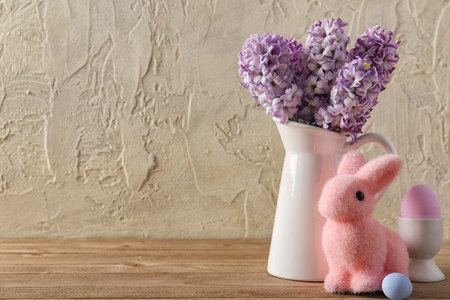 Vase with beautiful hyacinth flowers, painted eggs and Easter bunny on wooden table near grunge wallの写真素材