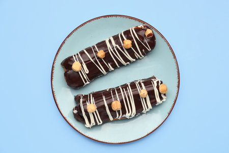 Plate with delicious chocolate eclairs on blue background