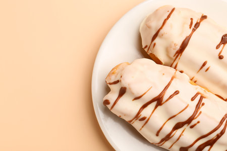 Plate with delicious eclairs on beige background