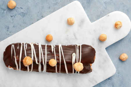 Board with delicious chocolate eclair and hazelnuts on gray table