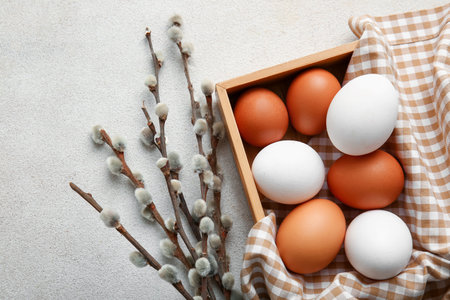 Wooden box with Easter eggs and willow branches on light background, closeup