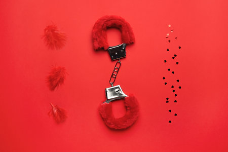 Handcuffs from sex shop, feathers and hearts on red background